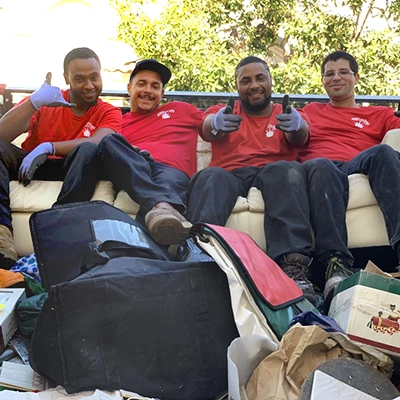 A smiling group of Junk King professionals sitting in the back of a truck.