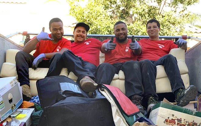 Row of smiling Junk King professionals sitting in the back of a truck.
