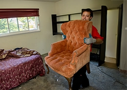 Junk King professional carrying an orange upholstered chair.