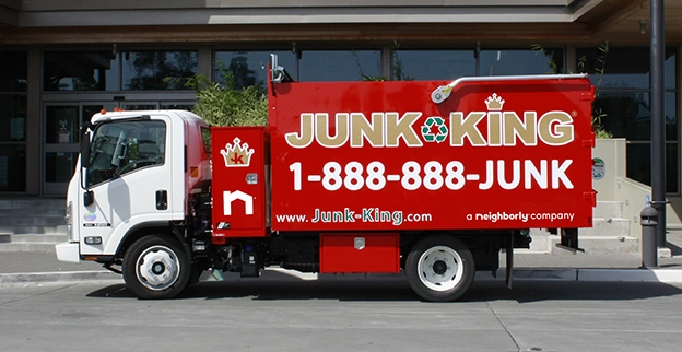 A branded Junk King dump truck parked in front of a school.