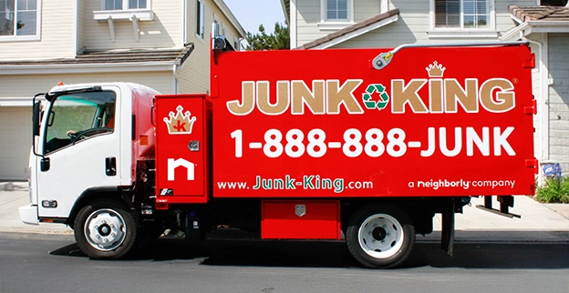 A branded Junk King dump truck parked on the street outside of a home.