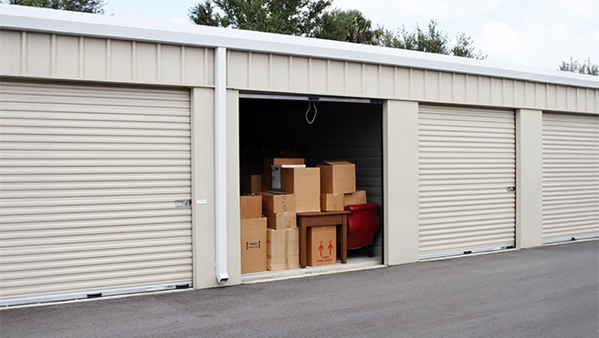 A storage facility with one door open, displaying a pile of cardboard boxes.