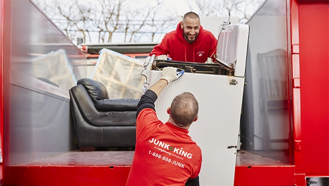 Junk King professionals loading a washing machine into the back of a truck.