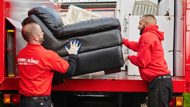 Junk King professionals loading a recliner into the back of a truck.