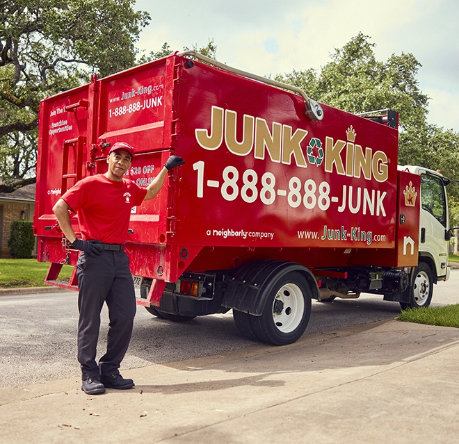 Junk King professional leaning against a red branded dump truck.