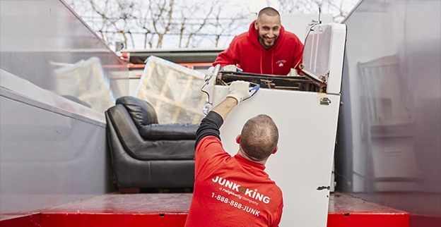 Two Junk King professionals loading a washing machine onto a truck bed.