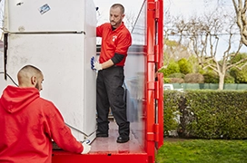Two Junk King professionals loading a refrigerator onto a truck bed.