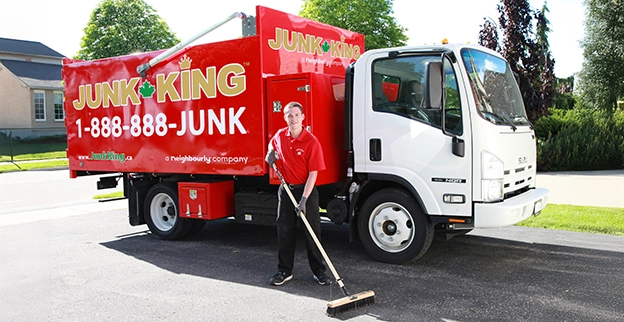 Red Junk King dump truck with an employee using a push broom beside it.