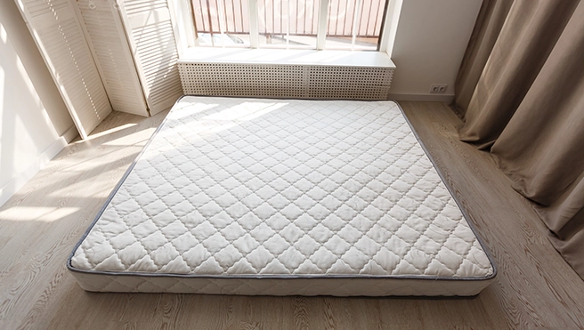 A white mattress on a bedroom floor.