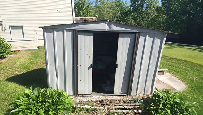 A metal shed with dents in it sitting in a yard ready to be demolished.