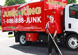 Red Junk King dump truck with an employee using a push broom beside it.