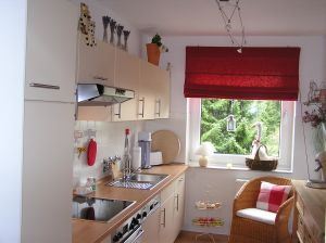 Small kitchen with cabinets, stove, and a window with red blinds.