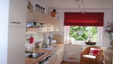 Small kitchen with cabinets, stove, and a window with red blinds.