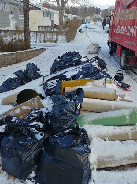 A truck parked in the snow, surrounded by bags of garbage waiting for collection.