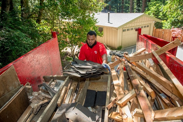 A man in a red shirt is loading wooden logs into the back of a truck.