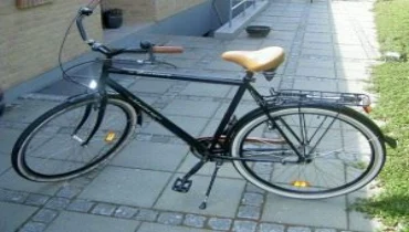 A black bicycle with a tan seat parked on a stone pathway.