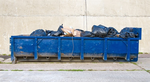A blue dumpster positioned in front of a textured wall.